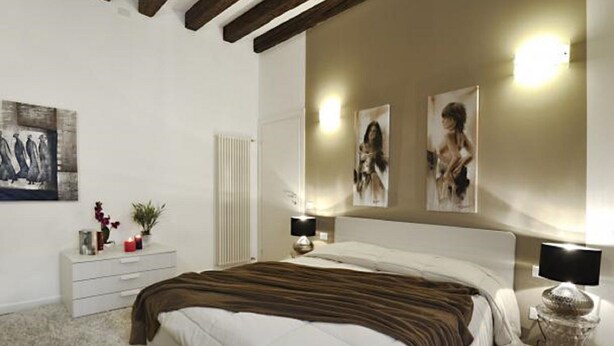 A bedroom with a large bed, bedside lamps, a white dresser, and artwork on the walls. - Rialto twins house, in the center of the city (Venezia)