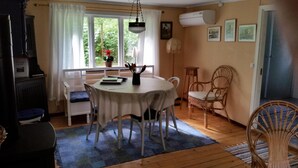 Un'accogliente zona pranzo con un tavolo rotondo, sedie bianche e una panca. Si vede una finestra con vista sul verde, un vaso con una pianta sul davanzale e una lampada a sospensione.