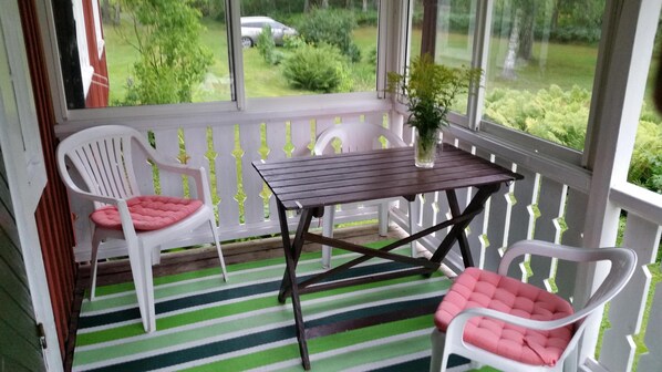 Une véranda avec deux chaises blanches dotées de coussins roses, une petite table en bois et une plante en pot.