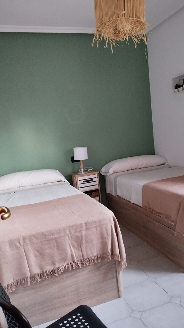 A room with two beds, a nightstand with a lamp, and a hanging light fixture.