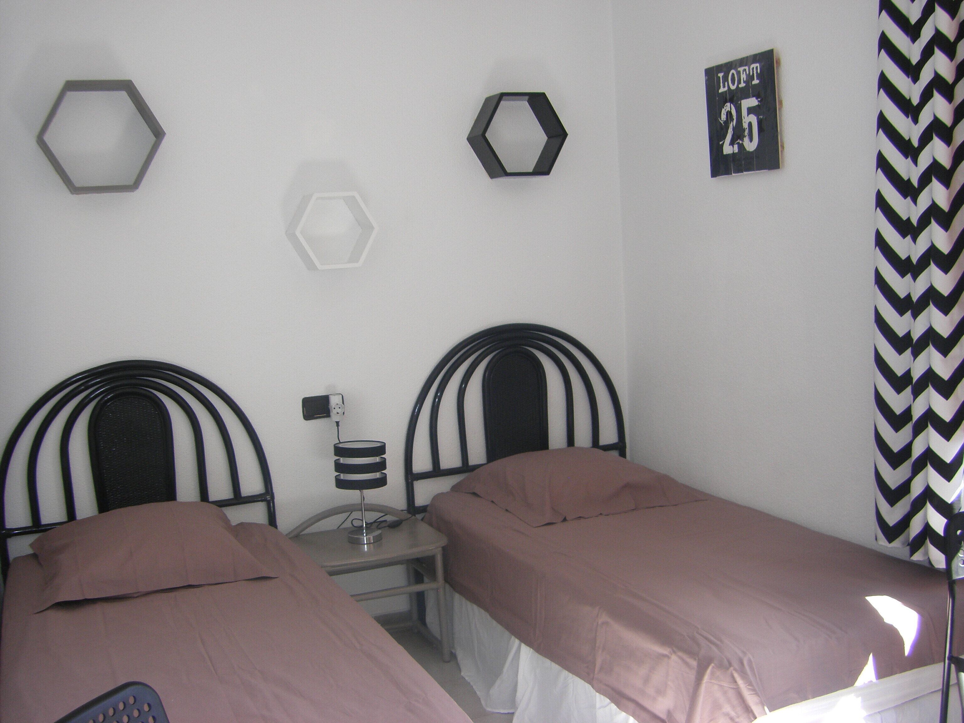 A room with two beds, a nightstand, a lamp, and a wall-mounted sign.