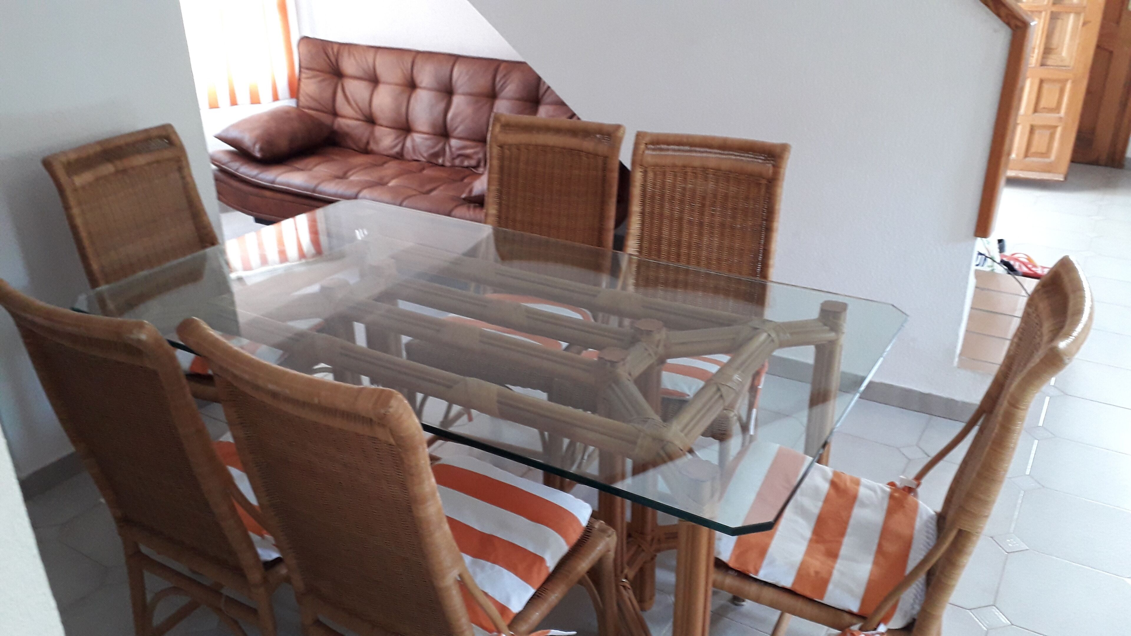 A dining area with a glass-top table surrounded by wicker chairs with striped cushions.
