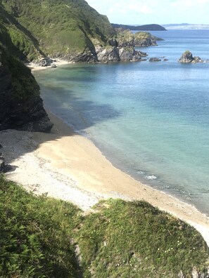 A coastal landscape with a sandy beach, rocky outcrops, and lush greenery.