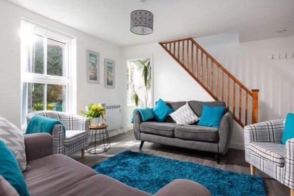 Un salon avec un canapé gris, un tapis bleu et un escalier.