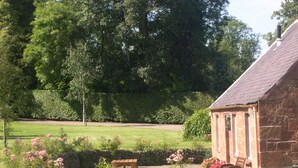 Un bâtiment en pierre doté d’un toit en pente, entouré d’un jardin bien entretenu avec des fleurs et une pelouse.