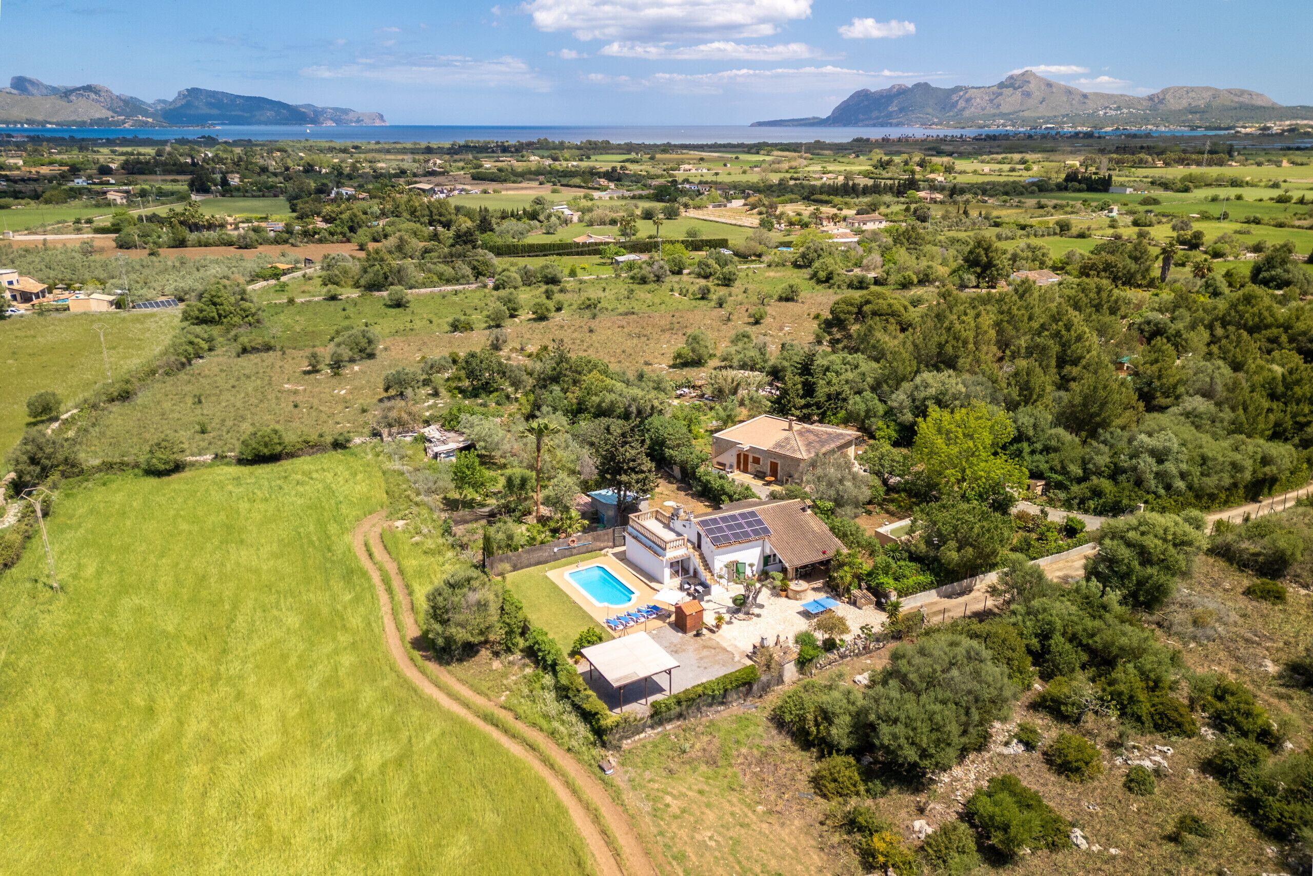 An aerial view of a property with a swimming pool, solar panels, and a large green field.