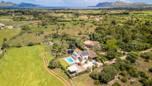 An aerial view of a property with a swimming pool, solar panels, and a large green field.