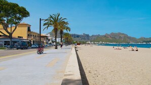 A beachside street with a sidewalk, palm trees, and a mountain backdrop.