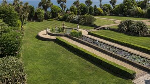 Ein gepflegter Garten mit Brunnen, Palmen und freiem Blick auf das Meer.
