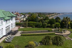 A large building with a green roof, a well-maintained garden with a circular fountain, and a view of the sea. - Luxury, award winning Art Deco house for special holidays and family events (Shanklin)