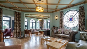 Ein geräumiges Wohnzimmer mit Billardtisch, Ledersofas und einem großen Fenster mit Buntglasdekor.
