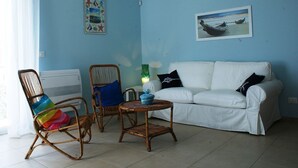 Une pièce avec un canapé blanc, deux fauteuils en osier, une petite table ronde et deux tableaux accrochés au mur.