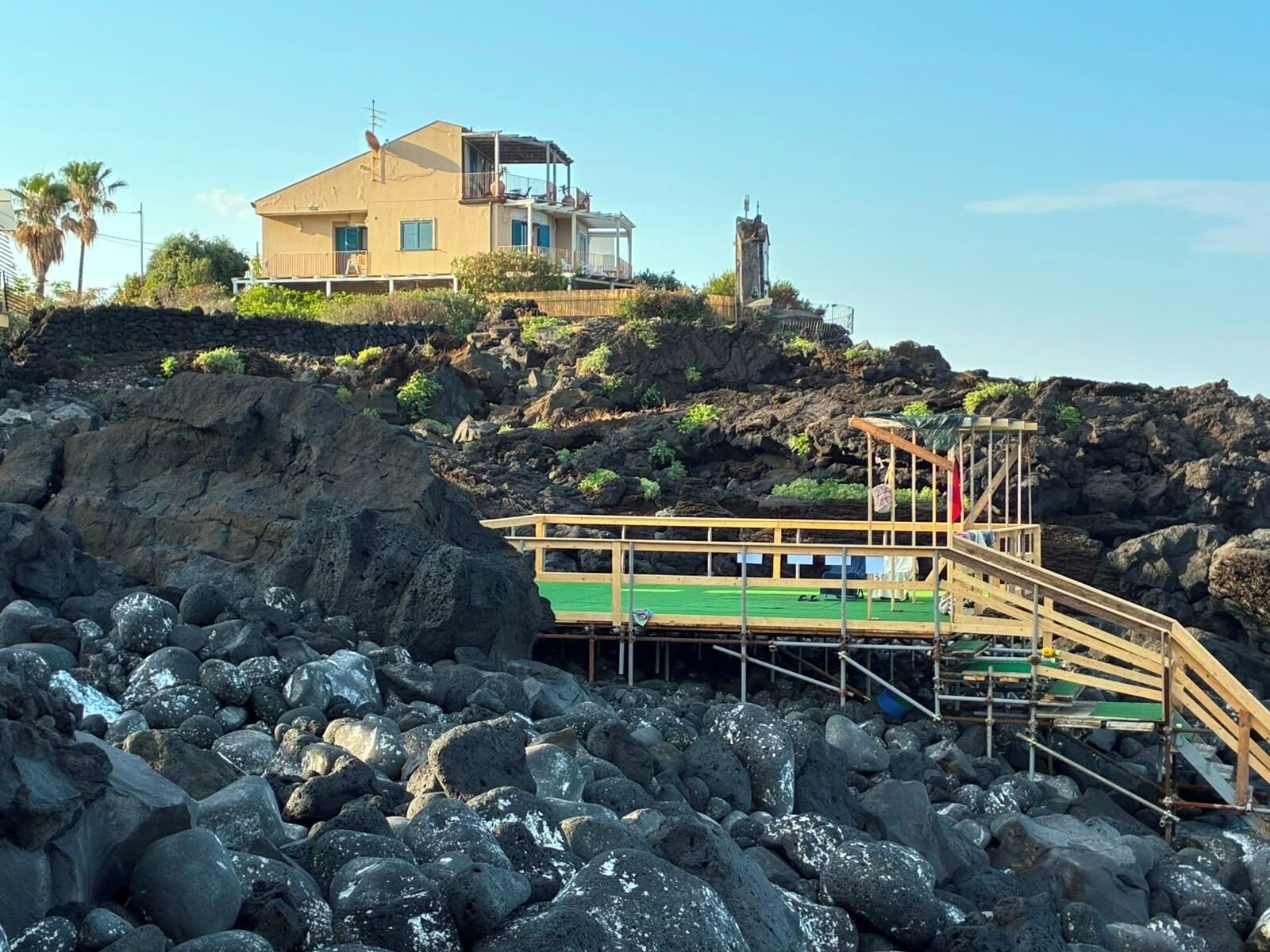 A coastal property with a wooden deck, a stone pathway, and a building with a balcony.