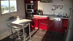 A compact kitchen with red cabinets, a double oven, a microwave, and a sink. - Très bel appartement Porticcio, vue mer sur le golfe d'Ajaccio (Grosseto-Prugna)