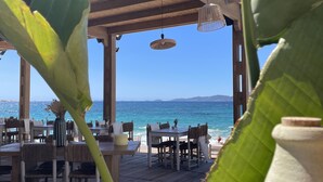 A restaurant with wooden tables and chairs, a thatched roof, hanging light fixtures, and a view of the ocean. - Très bel appartement Porticcio, vue mer sur le golfe d'Ajaccio (Grosseto-Prugna)
