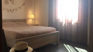 A bedroom with a bed, a nightstand with a lamp, a window with curtains, and a hat on the floor. - Très bel appartement Porticcio, vue mer sur le golfe d'Ajaccio (Grosseto-Prugna)