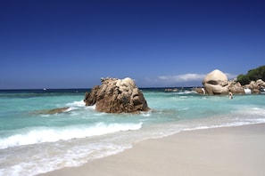 Ein Strand mit klarem türkisblauem Wasser, großen Felsen und einem Sandstrand.