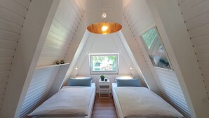 Quarto sótão triangular com duas camas, uma mesinha e uma janela com vista para o verde.