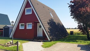 Um edifício vermelho com telhado inclinado, um pequeno alpendre e o número '66' na porta.