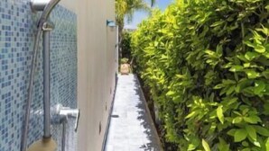 Un étroit sentier bordé d’un côté par une zone de douche carrelée et de l’autre par une haie.