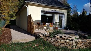 Uma casa com um pátio, mobiliário de exterior, um muro de pedra e um portão de madeira.