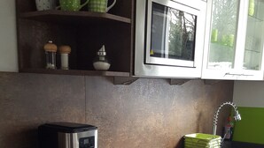Uma cozinha com cafeteira, micro-ondas e prateleiras com canecas.