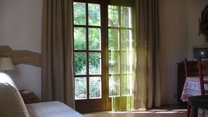 A room with a bed, a chair, a table with a lamp, a television, and a window with curtains. - Holiday house for 2 pesons on small Estate with pool, near hot springs (Civitella Marittima)