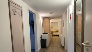 Un couloir avec un plancher en bois, une porte blanche avec un miroir, un radiateur et une petite poubelle.