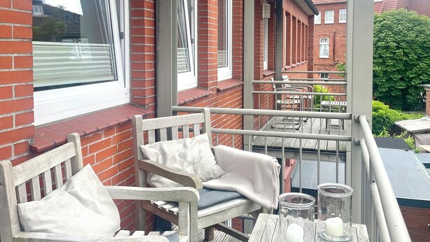 Un espace extérieur aménagé, abrité et doté de mobilier en bois et d’une table, avec un mur en briques et une pergola.