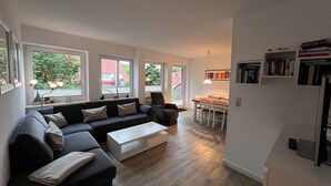 Un salon moderne avec un canapé foncé, une table basse blanche et un coin repas comprenant une table et des chaises en bois.