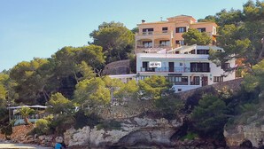 A multi-story building with balconies, situated on a cliff overlooking a turquoise sea. - Drac 5 by dracmallorca (Cala Santanyi)