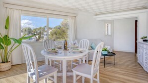 A dining area with a round table, white chairs, and a view of the outdoors. - Drac 5 by dracmallorca (Cala Santanyi)