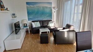 Sala de estar moderna com uma pintura grande de uma onda do oceano, um sofá, uma mesa de centro e uma TV sobre um suporte.