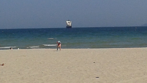 Uma praia com um barco ao longe e uma pessoa caminhando na areia.