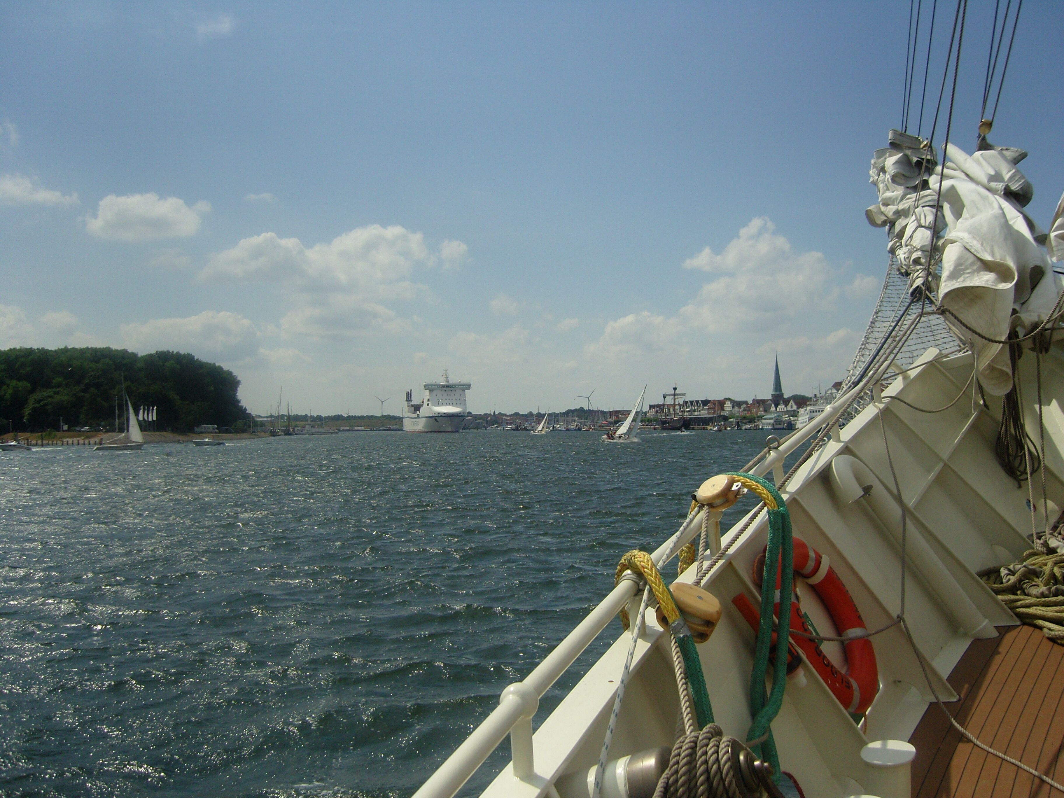 Uitzicht vanaf een boot, met een stadsgezicht op de achtergrond, inclusief een kerktoren en windmolens.