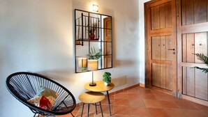 A room with a wooden door, a chair, a small table with a lamp, and a wall-mounted mirror with a plant. - Bassa Seca by dracmallorca (Santanyi)