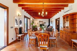 A spacious dining area with a wooden table and chairs, a chandelier, and a view of the outdoors. - Bassa Seca by dracmallorca (Santanyi)