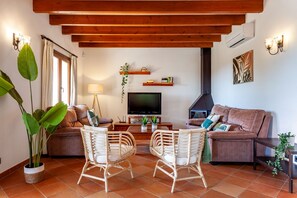 A living room with a sofa, two wicker chairs, a television, and a fireplace. - Bassa Seca by dracmallorca (Santanyi)