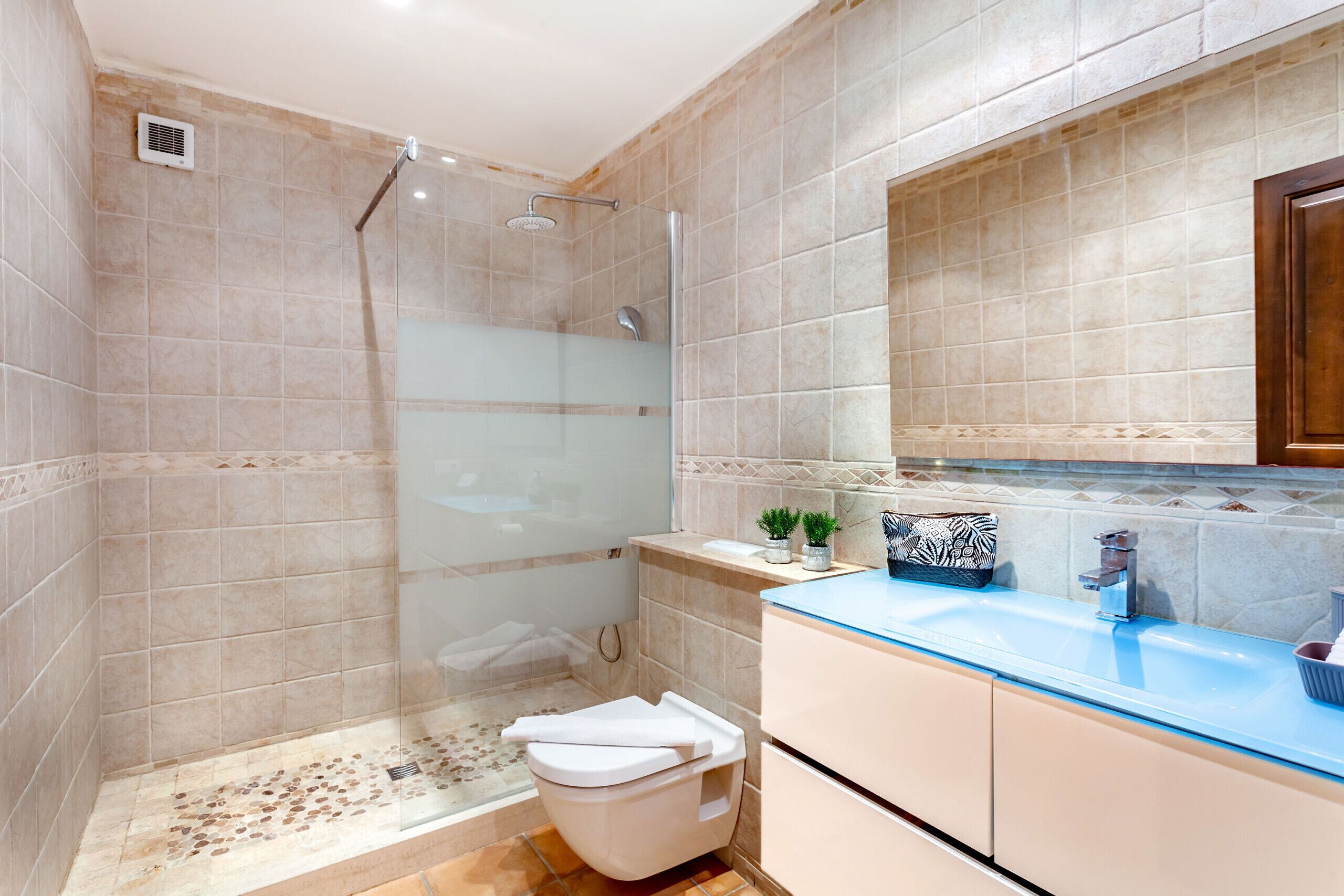 Ein Badezimmer mit einer gläsernen Duschkabine, einem Waschbecken mit blauer Ablage und einem Spiegel darüber.
