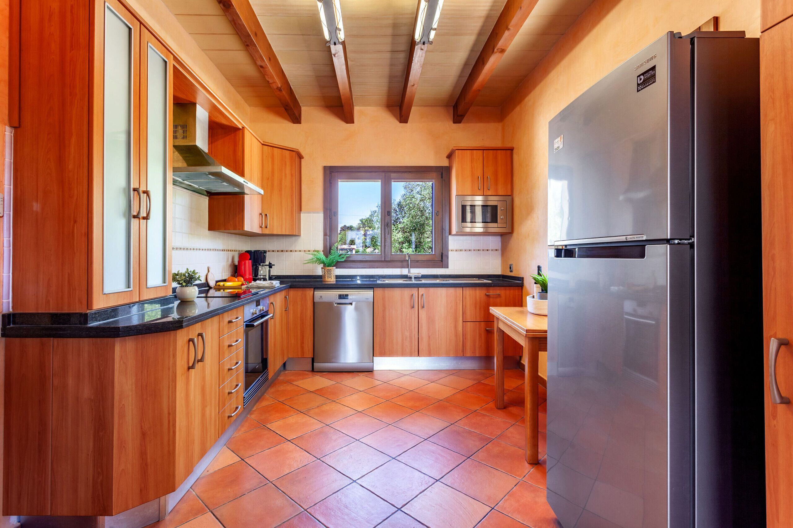 Een keuken met houten kastjes, een roestvrijstalen koelkast, een vaatwasser en een raam met uitzicht op groen.