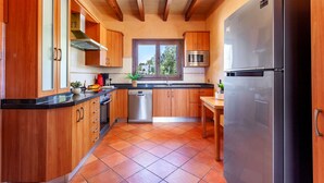 A kitchen with wooden cabinets, a stainless steel refrigerator, a dishwasher, and a window with a view of greenery. - Bassa Seca by dracmallorca (Santanyi)