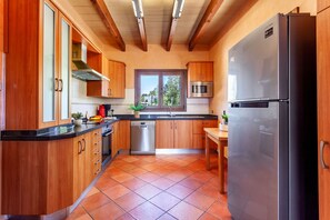 A kitchen with wooden cabinets, a stainless steel refrigerator, a dishwasher, and a window with a view of greenery. - Bassa Seca by dracmallorca (Santanyi)