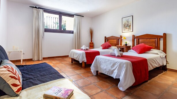 A hotel room with two beds, a window with curtains, a bedside table with a lamp, and a painting on the wall. - Bassa Seca by dracmallorca (Santanyi)