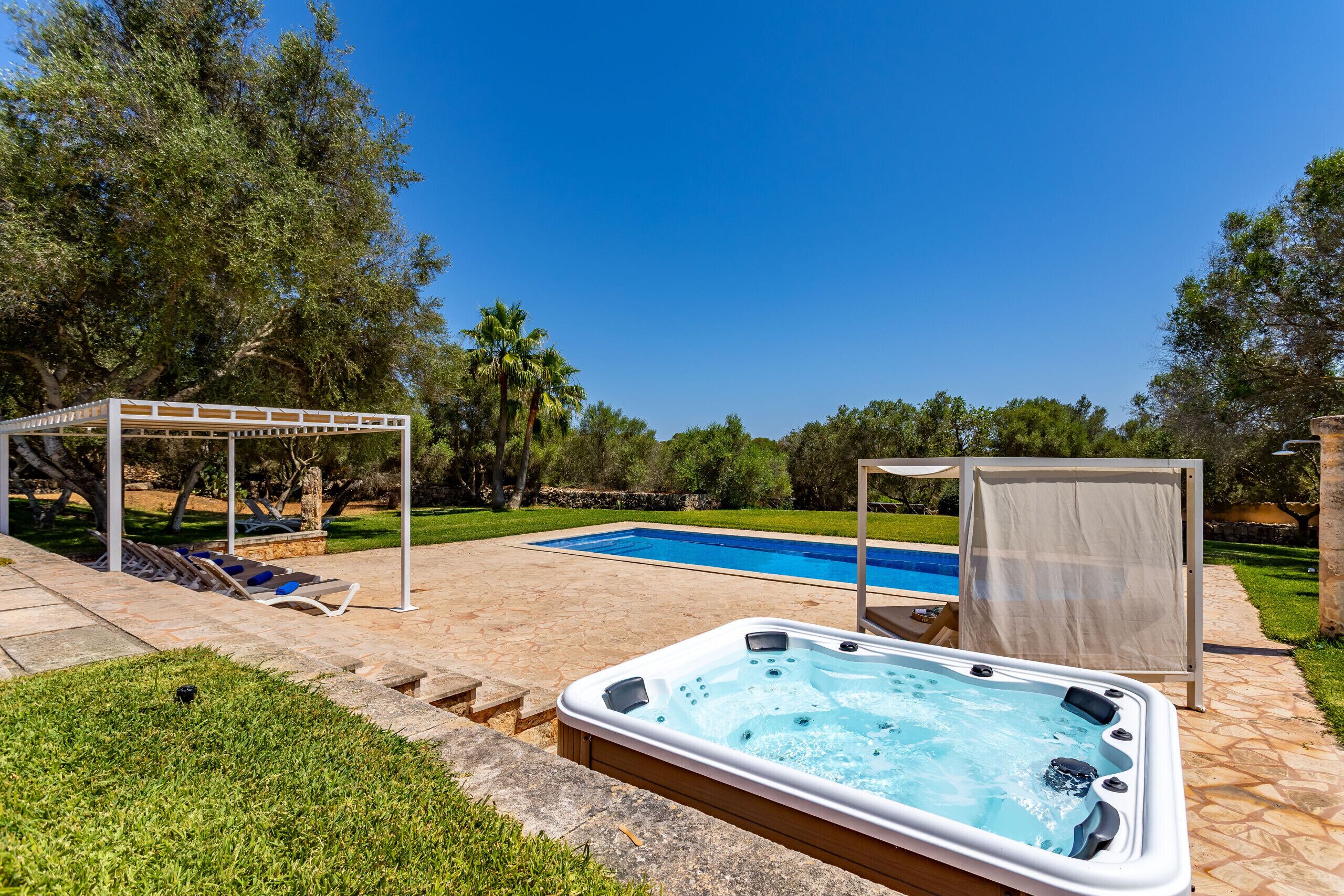 A backyard with a swimming pool, a hot tub, and a covered seating area.