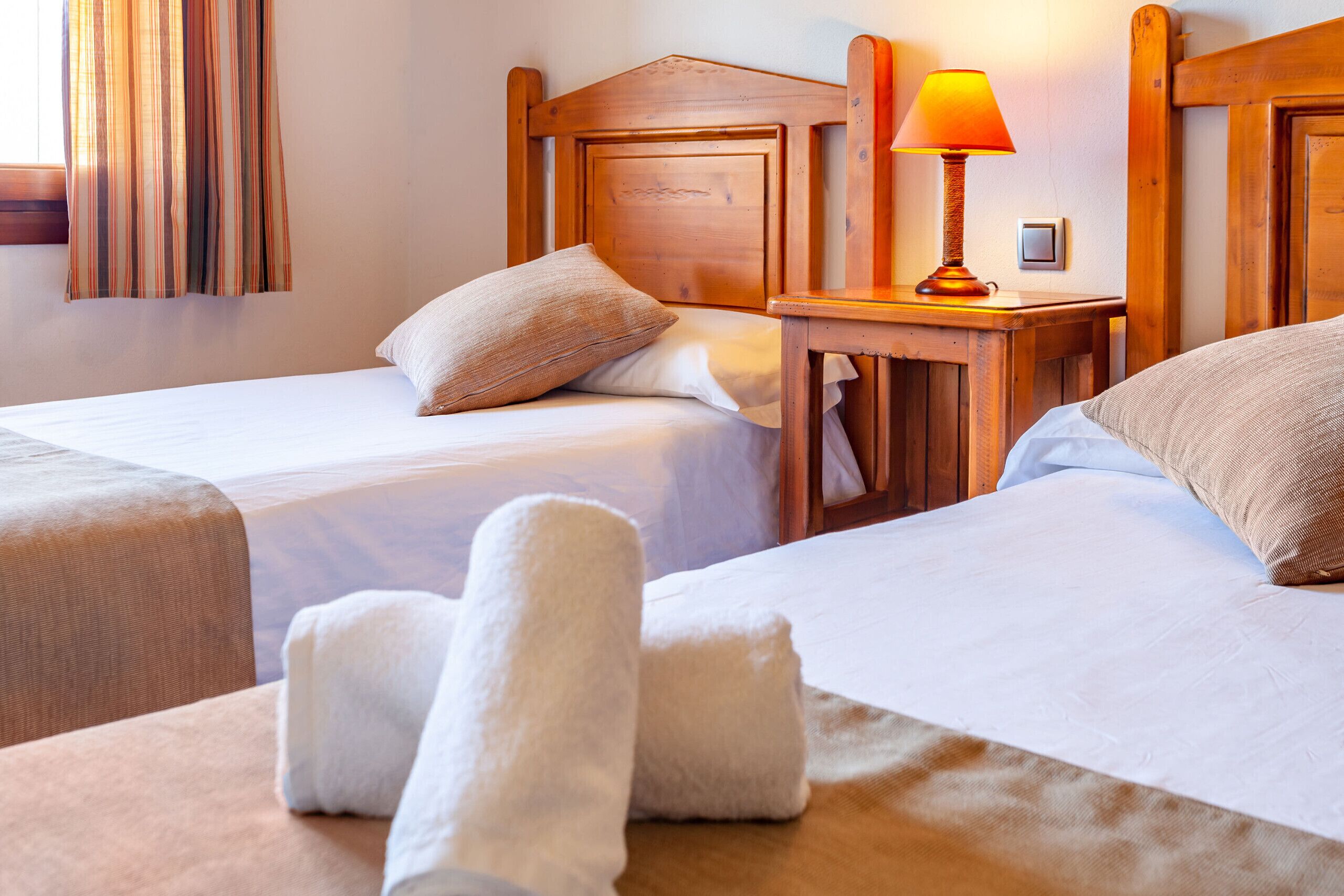 A hotel room with two beds, a wooden headboard, a bedside table with a lamp, and a towel on the bed.