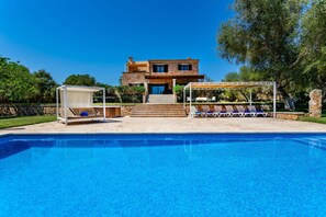 A pool with a pergola and lounge chairs, a stone house with a balcony, and a clear blue sky. - Bassa Seca by dracmallorca (Santanyi)