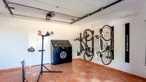 A room with a tiled floor, a door with a sign, a tripod stand, and bicycles mounted on the wall. - Bassa Seca by dracmallorca (Santanyi)