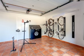 A room with a tiled floor, a door with a sign, a tripod stand, and bicycles mounted on the wall. - Bassa Seca by dracmallorca (Santanyi)