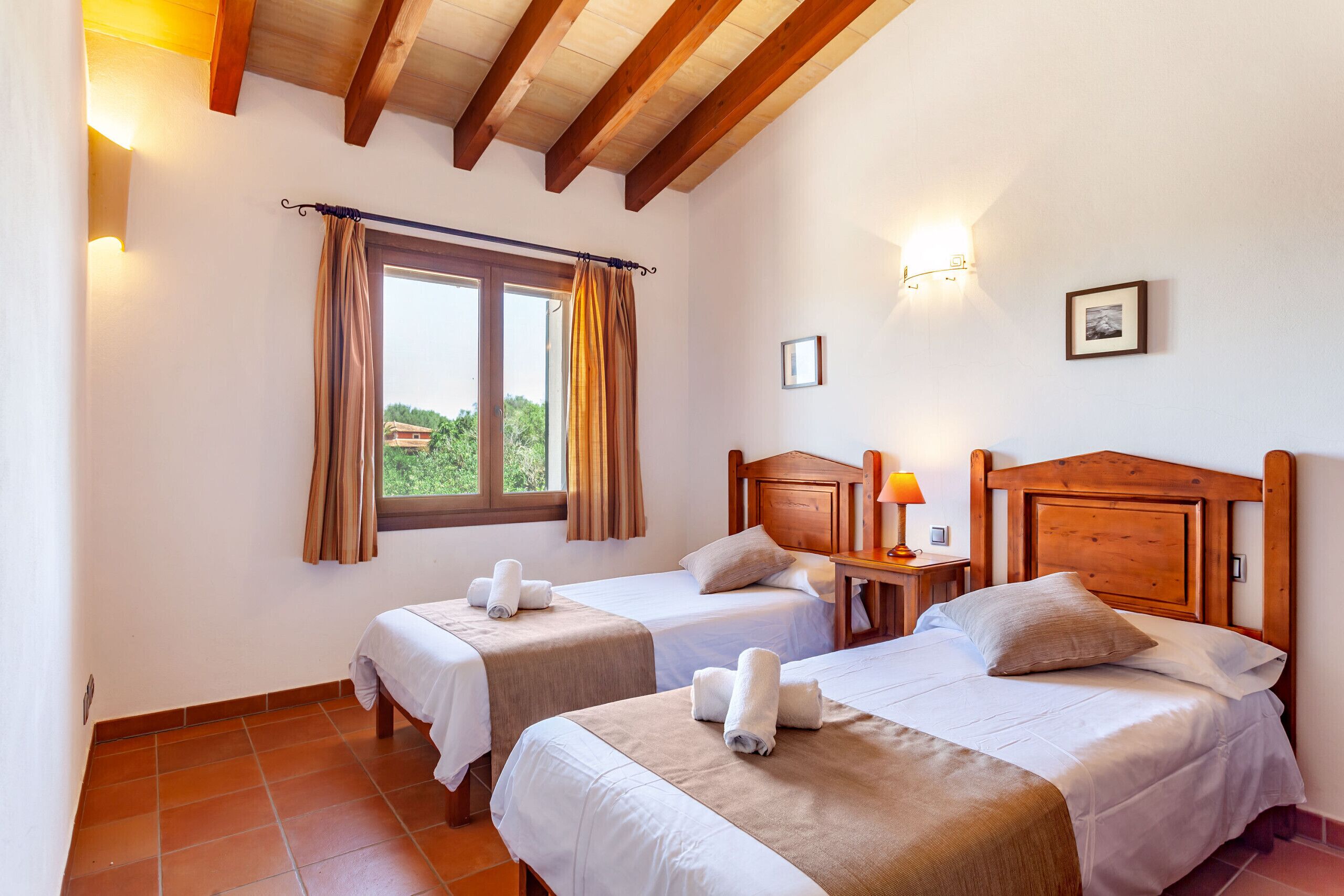 Une chambre d’hôtel avec deux lits, une fenêtre avec des rideaux, un plafond en bois et une lampe fixée au mur.