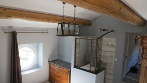 Ein Schlafzimmer mit Holzbalkendecke, einem Schminktisch, einem Fenster und einer Duschkabine.
